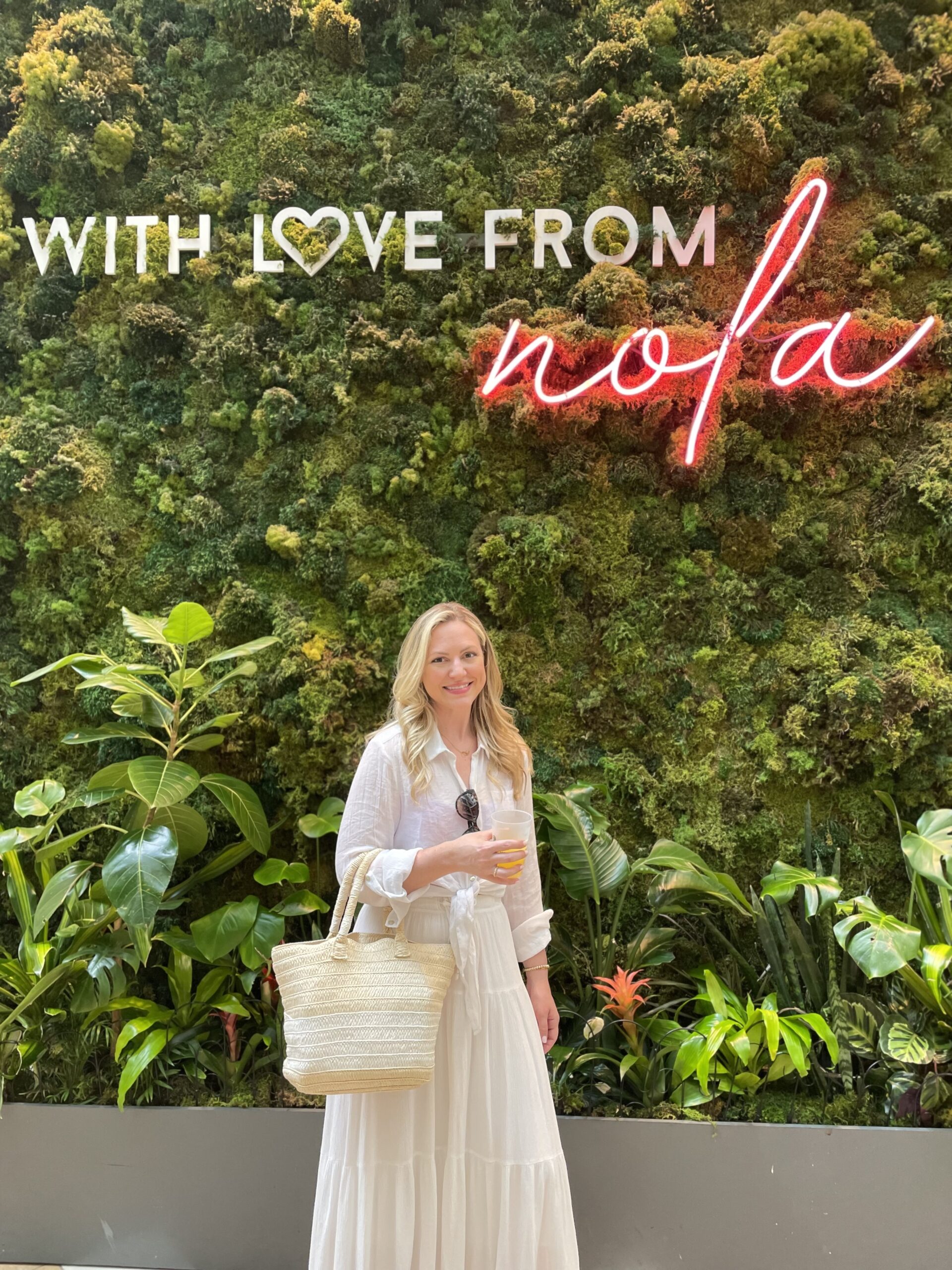 Girl in white outfit standing in front of green wall that says with love from nola